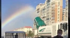 Lorry-mounted sprinkler leaves rainbow trail in the air behind it