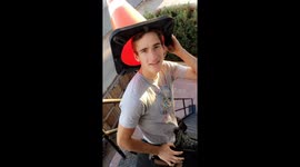 Kid puts a cone over his head and uses a suitcase to slide down a staircase