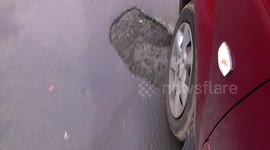 Pothole on road showing  wheel of car running over it.