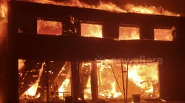 Close-up footage shows a burning building ravaged by Camp Fire