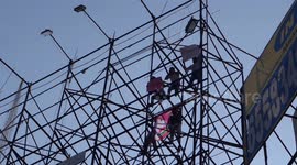Indian men scale a billboard scaffold in political protest