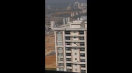 A lady steps out of her balcony into the dangerous area to clean the balcony