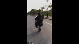 Two men riding a motorbike with a wheel on the busy road