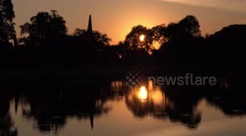 A beautiful sunset through trees, and over a pond.