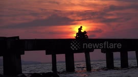 A man on a motorcycle at sunset takes selfies of a glorious sunset, to the soothing sound of the ocean waves.
