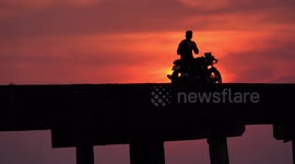 Two men and a motorcycle on a bridge at sunset, with the soothing sound of the ocean waves.