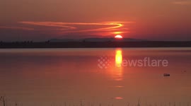 A beautiful sunset with orange sky and dragonflies, over tranquil water.