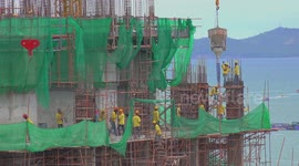 Construction workers on a building site, as tourists are enjoying ocean sports in the background.