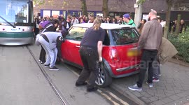 Bystanders lift a car off tramline in Nottingham, UK