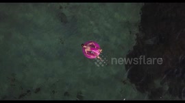 A young man on a flamingo shaped inflatable ride on pool toy floating in the middle of the emerald sea