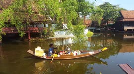 A lady sells refreshments and drinks from a boat at a floating market in Thailand.