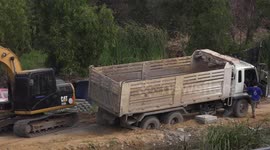 A truck with a load of sand gets stuck in the mud, an earth mover gives it a helping hand to unload the sand and get out of the rut.