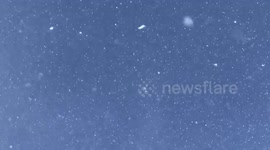 Heavy snow falling from a clear blue sky.