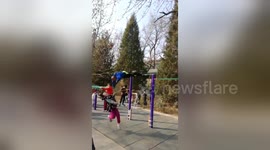 Old Chinese man swinging on horizontal bar knocks down girl walking by