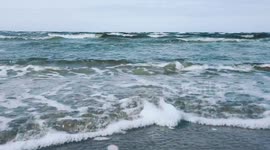 Blue sea waves crashing a sandy shore.