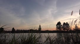 A large Buddha statue over looking a tranquil lake with long grass gently swaying in a gentle breeze.