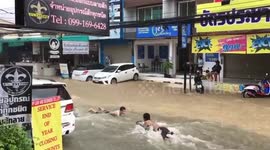 Boys go bodyboarding on flooded road in Thailand