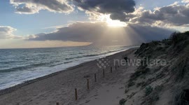 still shot of sun rays punching through clouds in a beach at sunset