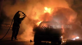 A car is burning and gasoline is dripping and burning. Firefighter sprays water and foam for extinguishing the fire