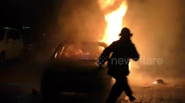 A car is burning and gasoline is dripping and burning. Firefighter sprays water and foam for extinguishing the fire