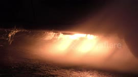 A car is burning and gasoline is dripping and burning. Firefighter sprays water and foam for extinguishing the fire