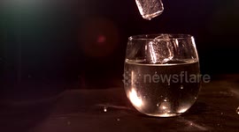 super slow motion ice dropping in to glass of water with dark background