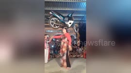 Woman dances in front of crowd with MOTORCYCLE on her head