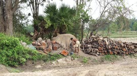 Charcoal man retrieving freshly made charcoal from a dried mud mound in Thailand.