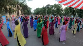 Hundreds of people wear long dress in many colors dancing on the street.