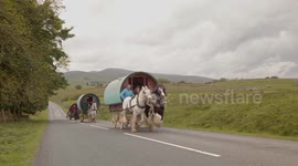 Travellers drive their horse-drawn caravans up steep hill on their way to Appleby Horse Fair