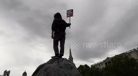 Protester holds 'Dump Trump' sign aloft atop statue in Trafalgar Square