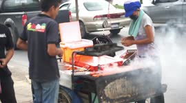 A street vendor in Thailand selling barbecued chicken by the side of a busy street.