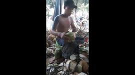 The man uses a knife to peel the coconut very quickly