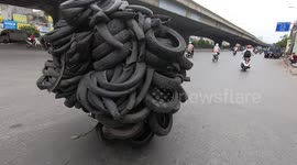Hundreds of tyres are balanced on motorbike as it drives down road in Vietnam