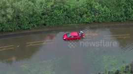 Drone footage shows two men pushing their car through submerged UK road