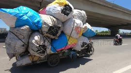 Man driving overloaded tricycle carrying dozens of giant sacks