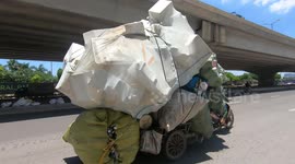 Dangerously Overloaded Transports: Man driving overloaded tricycle carrying bulky foam boxes and giant sacks.