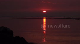 A beam of light from a setting sun across the ocean fades away and turns to darkness.