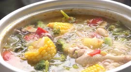 A pot of chicken and vegetable soup bubbling and gurgling as its being cooked.