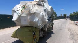 Ridiculously overloaded! Man driving an overloaded tricycle carrying bulky foam blocks and huge sacks