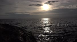 The ocean waves crash into a rocky beach at sunset creating a very relaxing sound.
