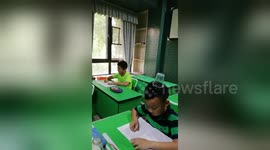 Chinese pupils balance plastic cups on heads while practising their handwriting