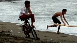 a child in the city of Padang relaxes on his bicycle without falling to see his friends practice surfing on the beach in the city of Padang