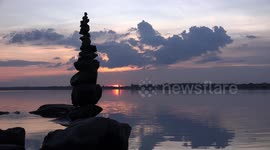 A time to reflect across a lake at sunset after building a tall balanced tower of stones.