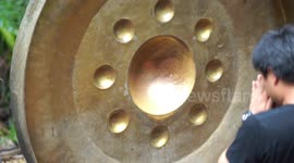 People at a Thai Buddhist temple try to make a large gong resonate so that they will be lucky in life.