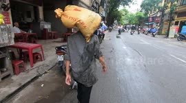 A Vietnamese woman skillfully balanced her 30 kg rice sacks on her head while walking on the street.