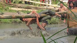 Contestants whack each other with bags of rice while balancing on pole over pool of mud in Indonesia