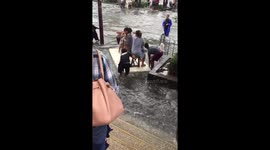 Women float on polystyrene board across road flooded by Storm Bailu