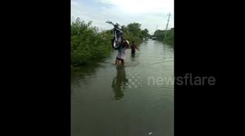 Indian man carries motorbike on shoulder over flooded road so it doesn't get wet