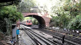 An incoming train passes under a bridge in a rainy day, moments before the sun sets